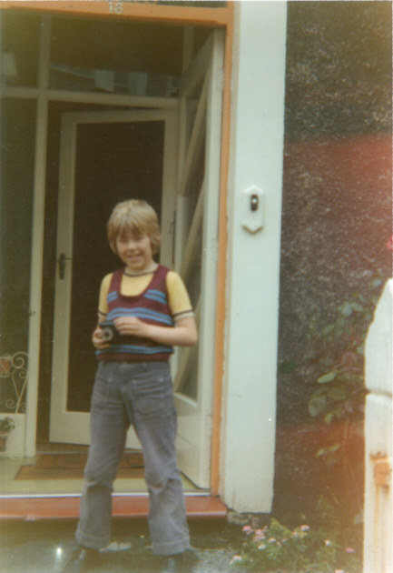 Picture of boy holding a camera standing in front of a house door