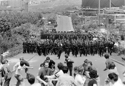 Photo of a mass charge of police down a village road towards a group of miners