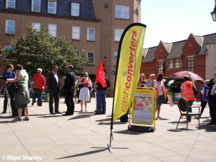 Photo of the preparations for a march against low pay, with the advertising of 'Cash Converters' right in the middle of shot